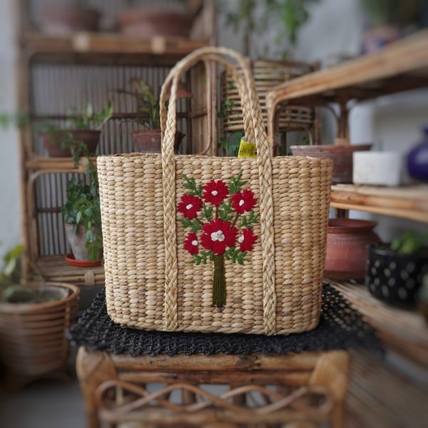 a hand woven straw or kauna handbag or tote bag with flowers embroidered on it